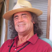 Man with long dark hair wearing a straw hat and red shirt